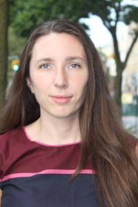 A woman with long hair and a striped shirt with trees in the background